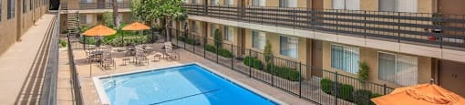 a hotel pool with umbrellas and tables and chairs at Villa La Paz Apartments, Bellflower, CA, 90706