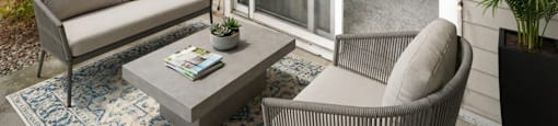 A patio with a grey sofa, a grey coffee table, and a chair with a plant on the side.