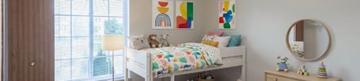 A child's bedroom with a white bed, a wooden dresser, and a round mirror on the wall.