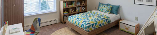 A bedroom with a bed, chair, and bookshelf.