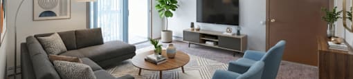 A living room with a grey couch, blue chairs, and a flat screen TV.