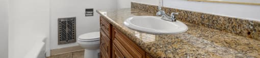 Apartments for Rent in Van Nuys CA - Colonial Manor - White Bathroom with Tub, Toilet, Granite Sandy Vanity, Mirror, and Tan Cabinetry