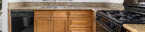 Van Nuys CA Apartments for Rent - Colonial Manor - Traditional Kitchen with Black Appliances, Sandy Countertops, Dark Tan Cabinetry, Window, and Overhead Lighting