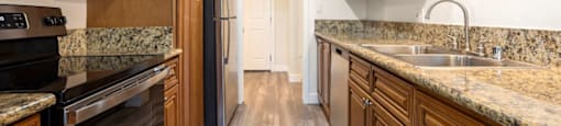 Encino CA Apartments - White Oak Terrace - Interior View Of Kitchen Featuring Brown Wooden Cabinetry and Stainless Steel Refrigerator, Oven Stove, and Microwave With Beige Granite Countertop