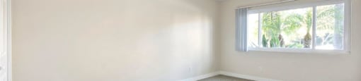 Apartments in Encino - White Oak Terrace - Interior View Of Bedroom Featuring Beige Carpets And Large Window Outlooking Palm Trees