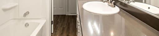 A white bathroom with a tub, sink, and mirror at The Reserve at Warner Center Apartments, Woodland Hills, CA 91367
