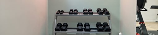 a rack of dumbbells in a gym with a clock on the wall