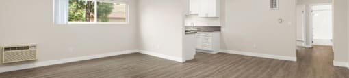 an empty living room with a kitchen in the background