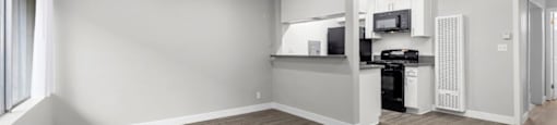 an empty living room with a kitchen in the background