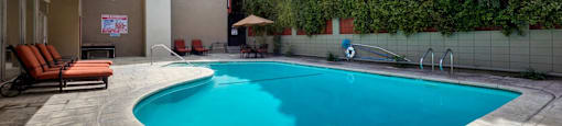 Apartments in Encino for Rent - White Oak Terrace - Exterior View Of COmmunity Pool Featuring Orange Lounge Chairs On Top Of Stone Deck With Large Lush Green Tree Privacy Wall