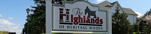 A sign for The Highlands of Heritage Woods is surrounded by flowers. at Highlands of Heritage Woods Apartments, Copley 44321