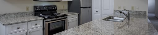 A kitchen with granite countertops and white cabinets. at Highlands of Heritage Woods Apartments, Copley, Ohio
