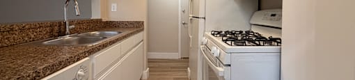 A kitchen with white appliances and a brown granite counter.