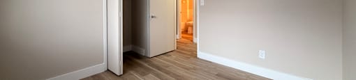 A room with a wooden floor and a white wall with a doorway leading to another room.