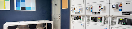 a laundry room with a table and chairs and a row of white washers and dryers at Nextloft Apartments, South Carolina, 29910