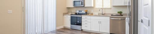Model kitchen at Village Green of Queen Creek with wood-style flooring, modern appliances and a sliding glass door