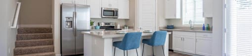 An open concept kitchen has an island with two stools in an apartment at Village Greens of Queen Creek