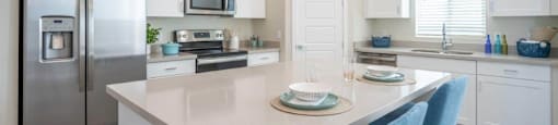 An island with 2 stools sits in the middle of a kitchen with stainless steel appliances at Village Greens of Queen Creek