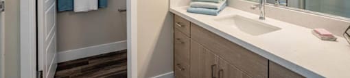 Model bathroom has a long mirrored vanity sink with storage in an apartment at Village Greens of Queen Creek