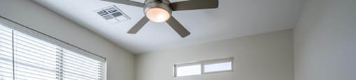 A carpeted bedroom has a window and ceiling fan in an apartment at Village Greens of Queen Creek