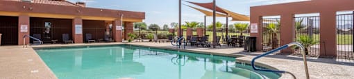 The pool is surrounded by a sundeck with lounge chairs at Village Greens of Queen Creek