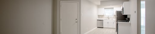 an empty room with a kitchen in the background