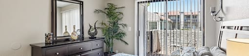 A bedroom with a bed, dresser, mirror, and a plant.