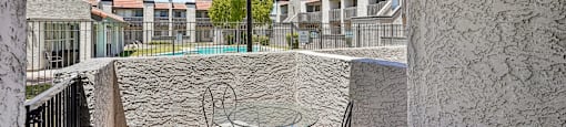 A patio with a table and chairs overlooks a pool and apartment buildings.