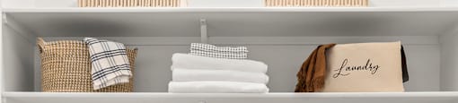 Two white washing machines with towels and baskets on top.