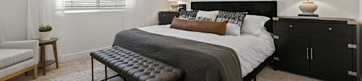 A bedroom with a large bed, a bench, and a ceiling fan.