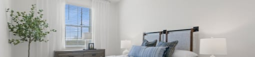 A bedroom with a bed, nightstand, and a plant.
