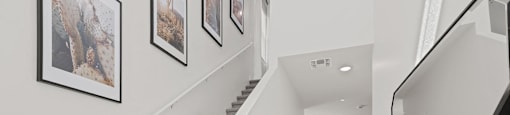 A staircase with a beige carpeted runner and white walls with framed pictures.