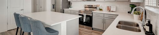 A modern kitchen with a white island and grey chairs.