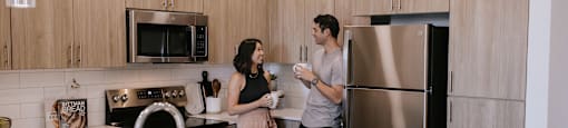 Two people standing in a kitchen with a sink and refrigerator.