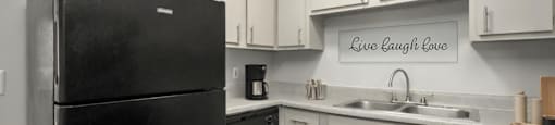 A black refrigerator in a kitchen with a sign that says Live Laugh Love.
