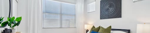 A bedroom with a large bed, a ceiling fan, and a window with blinds.