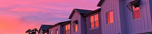 A row of houses with garages are shown at dusk.