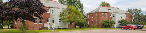 A parking lot with a red car and two buildings in the background.