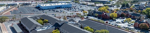A large building with a grey roof is surrounded by a parking lot and other buildings.
