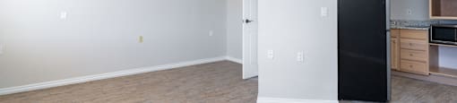 A room with a black fridge and wooden floors.