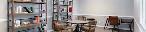 A room with a white ceiling, a table, chairs, and bookshelves.
