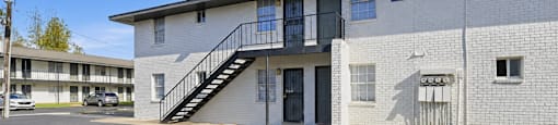 A parking lot in front of a white building with a black staircase.