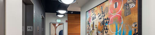 A hallway with a large painting on the wall and a door on the left.