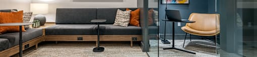 A modern office space with a grey sofa, orange pillows, and a glass wall.