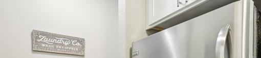 A stainless steel refrigerator and washing machine in a laundry room.