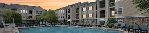 A pool surrounded by chairs and apartment buildings in the background.