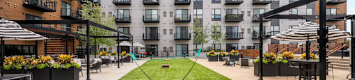 A grassy area in front of apartment buildings with a putting green and a few chairs.