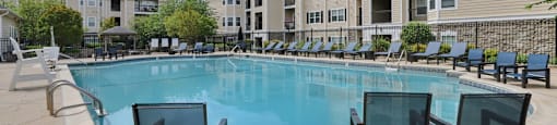 A swimming pool surrounded by lounge chairs and apartment buildings in the background.