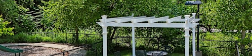 A white pergola is in the middle of a green park.