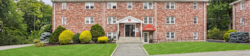 A large red brick building with a red roof and a driveway leading to the front door.